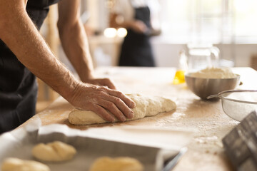 Baker's hands rolling out raw dough in bakery