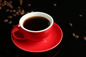 Red cup with coffee and roasted beans on black background, closeup