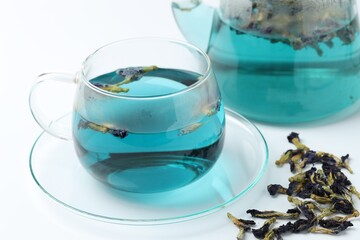 Fresh butterfly pea flower tea in cup and dry petals on white table, closeup