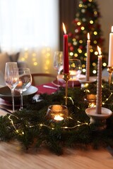 Festive table setting in room decorated for Christmas, closeup. Bokeh effect