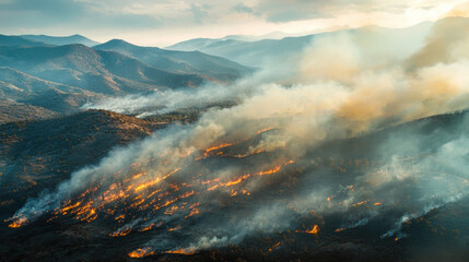 Fototapeta premium Aerial view of a forest fire burning through a dry mountain landscape, with thick smoke drifting over the peaks and the fireline glowing vividly