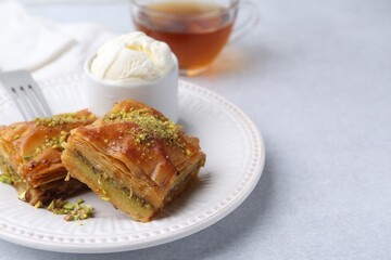 Delicious baklava with crushed nuts and ice cream on grey table, closeup. Space for text