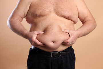 Naklejka premium Man with excessive belly fat on beige background, closeup. Overweight problem
