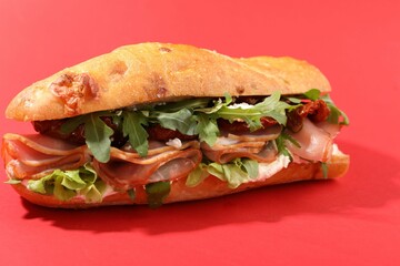 Baguette sandwich with ham and sun dried tomatoes on red background, closeup