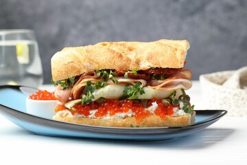 Delicious baguette sandwich with caviar, ham and capers on white wooden table, closeup