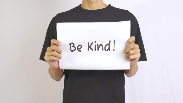 a footage of a man standing holding a paper that says be kind