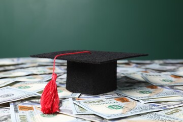 Graduate hat on dollar banknotes, closeup. Tuition payment