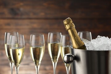 Bottle of sparkling wine in cooler bucket and glasses against wooden background, closeup
