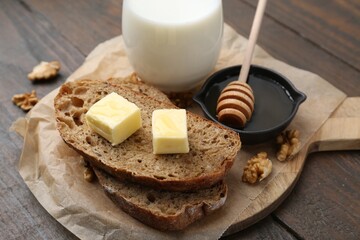 Slices of bread with butter, honey, milk and walnuts on wooden table, closeup