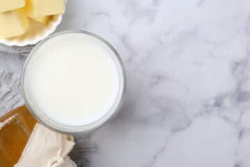 Fresh milk in glass, honey and butter on white marble table, flat lay. Space for text