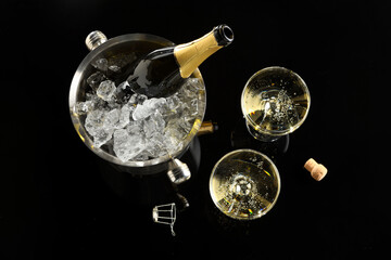 Bottle of sparkling wine in cooler bucket and glasses on black table, flat lay © New Africa