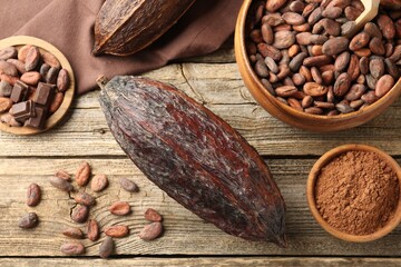 Cocoa pod, powder and beans on wooden table, flat lay