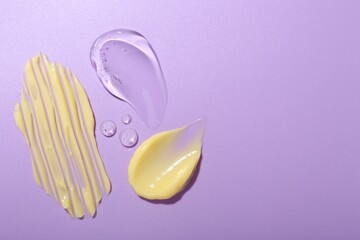 Cream and gel samples on violet background, flat lay. Space for text