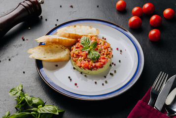 Guacamole tartare with fresh vegetables, basil garnish, and crispy baguette slices on a white plate