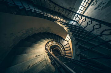 A captivating spiral staircase leads downwards, showcasing intricate railings and soft lighting in a rustic, atmospheric setting.