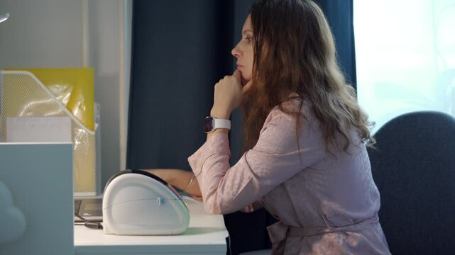 woman in a pink robe sits at a desk in a home office, using a thermal label printer to print labels.