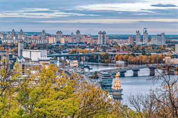 Obraz premium Scenic view of Kyiv, Ukraine, showcasing the city's architecture and bridges over the Dnipro River during the autumn season. Photo captures a vibrant mix of urban landscape and colorful fall foliage