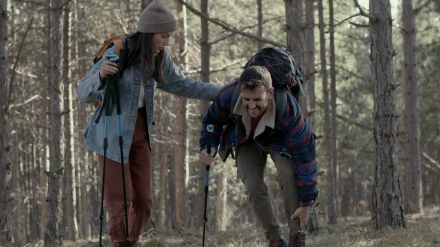 A man in pain holding his ankle as a worried woman stays by his side on a forest path. 4k video