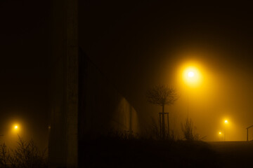 Urban sidewalk with massive concrete wall at night lit by orange sodium vapour street lights