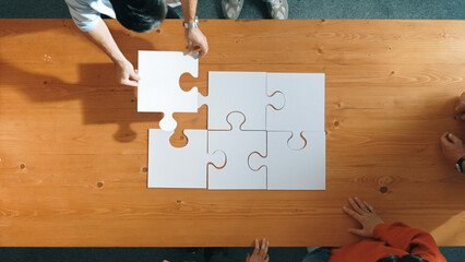 Top down view of skilled business people assemble jigsaw puzzle on meeting table. Group of diverse...