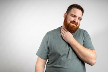 Obraz premium young bearded man feeling ill with a sore throat and flu symptoms, coughing with mouth covered against grey wall