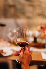 Hand holding a glass of red wine at a cozy dinner gathering with candles and elegant table decor