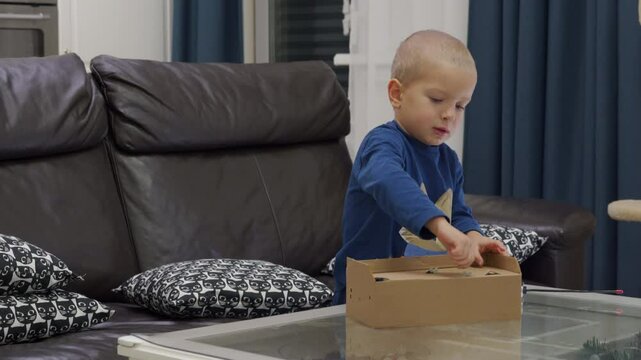 Impatient child unboxing new toy at home. Excited little boy unpacks remote-controlled transformer car.