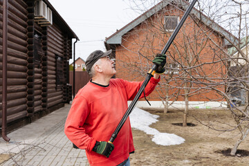 Gardener reaching for tall branches with telescopic pruning shears in a backyard garden