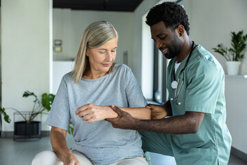 Obraz premium African American male doctor hand doing physical therapy by extending elbow of mature female patient