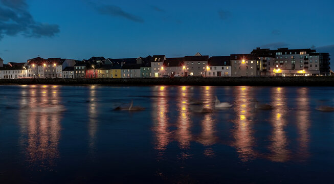 Late evening view of The Long Walk in Galway, with swans gliding in motion blur on the river.