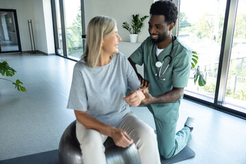 Fototapeta premium African American male doctor hand doing physical therapy by extending elbow of mature female patient
