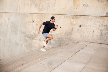Young man in sportswear running up stairs near marina during fitness session