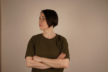 Obraz premium A brunette girl with short hair and gray eyes. She crossed her arms in front of her and looks in the other direction. The girl is found. On a beige background.