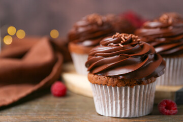 Tasty cupcakes with chocolate cream and raspberries on wooden table, closeup. Space for text