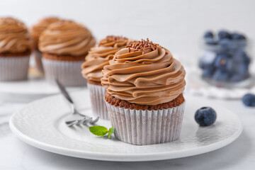 Tasty cupcakes with chocolate cream and blueberries on white marble table, closeup