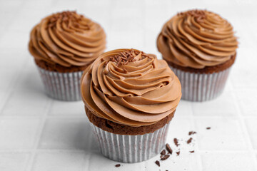Tasty cupcakes with chocolate cream on white tiled table, closeup