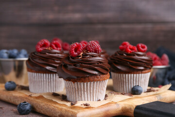 Tasty cupcakes with chocolate cream and berries on brown table, closeup