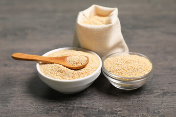 Oat bran in bowls, burlap bag and spoon on grey table, closeup