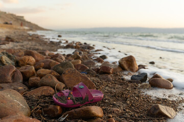 Old slippers lying on contaminated beach, symbolizing human impact on nature. Ecological campaigns, sustainability projects, and awareness articles.