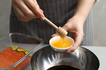 Woman adding honey into bowl with soy sauce at gray table, closeup