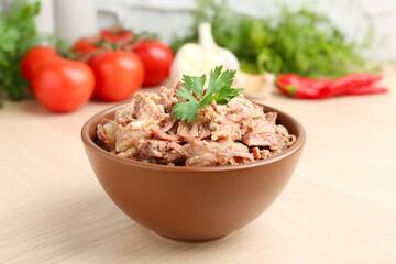 Canned meat with parsley in bowl on wooden table, closeup