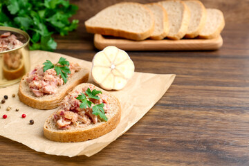 Sandwiches with canned meat, parsley, garlic and peppercorns on wooden table, closeup. Space for text