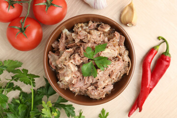 Canned meat in bowl, parsley, tomatoes, garlic and chili peppers on wooden table, top view