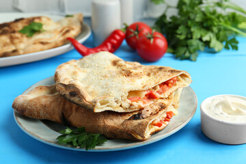 Halves of tasty calzone with meat, cheese, tomato and sauce on light blue table, closeup