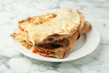 Halves of tasty calzone with meat, cheese and tomato on white marble table, closeup
