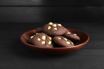 Delicious chocolate cookies with hazelnuts on black wooden table, closeup