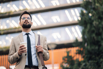 Confident businessman holding coffee walking outside office building
