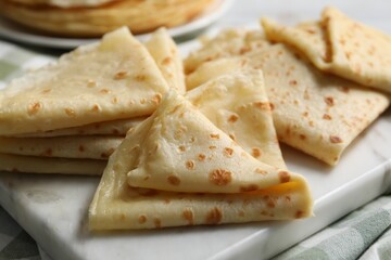 Many tasty crepes on white marble board, closeup