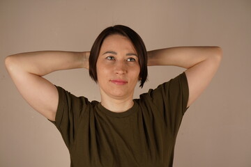 Portrait of a worried brunette looking to the side with her hands behind her head. She stands by...