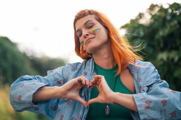Young activist showing heart sign with rainbow makeup supporting lgbtq plus community